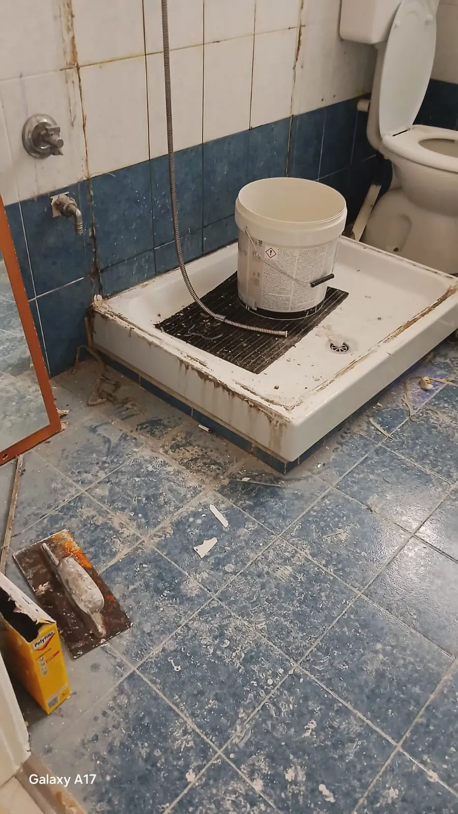 Bagno con piastrelle blu prima dell'intervento: detriti e residui di cantiere sul pavimento